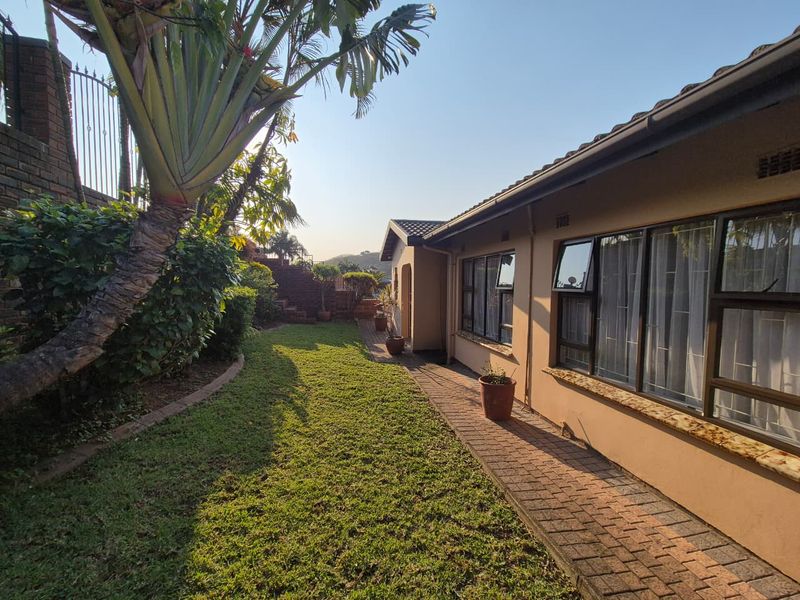 A view of the rear exterior of the house featuring a paved walkway, well-maintained lawn, and aluminium-framed windows along the side elevation.