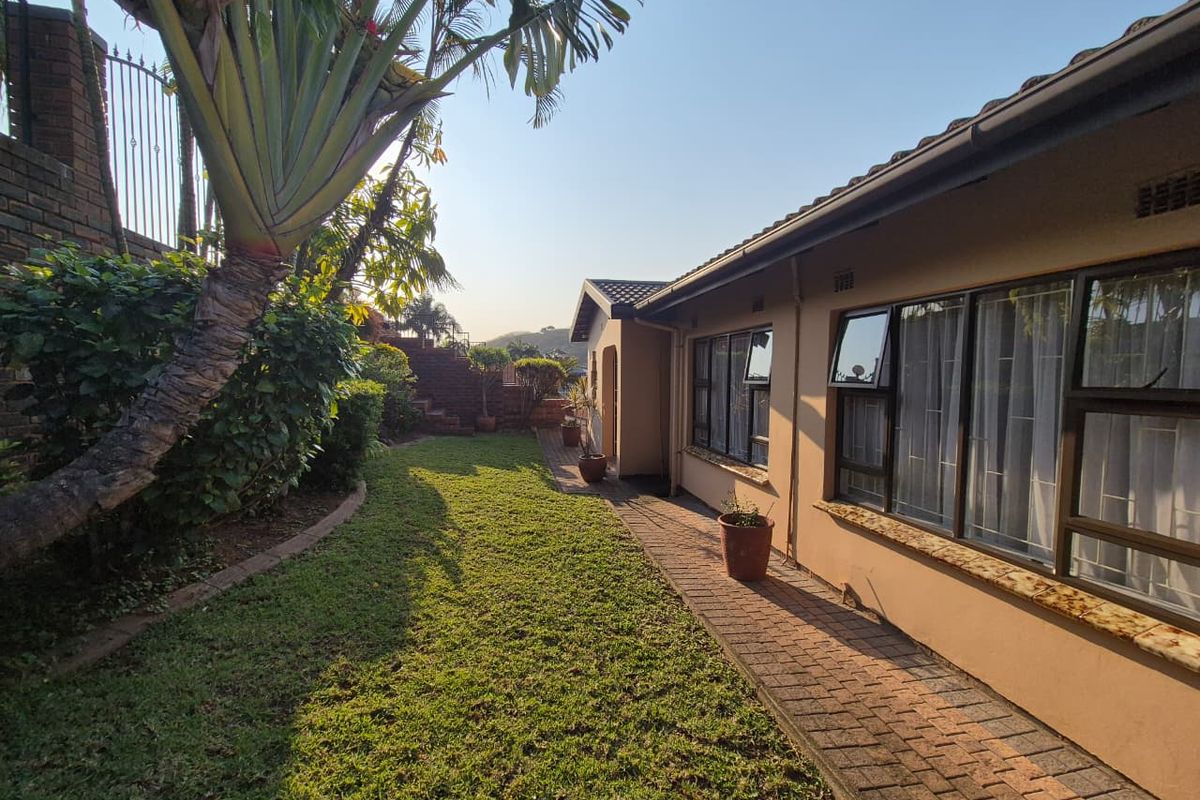 A view of the rear exterior of the house featuring a paved walkway, well-maintained lawn, and aluminium-framed windows along the side elevation.