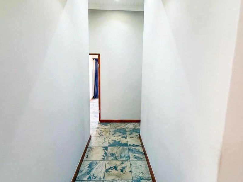 A clean, empty hallway featuring tiled flooring, recessed downlighting, and neutral wall finishes, providing a bright transition space between rooms.