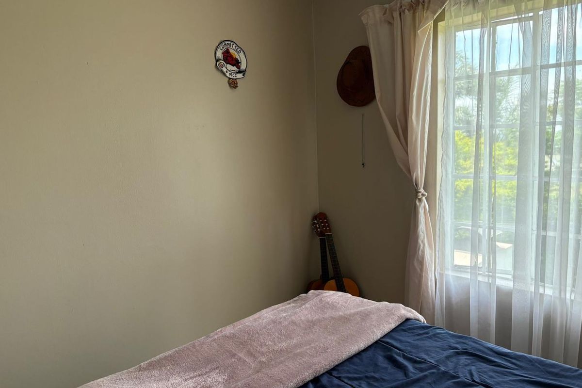 A bedroom featuring neutral wall tones, a window with security bars, and decorative cove cornicing, offering a simple and functional living space.