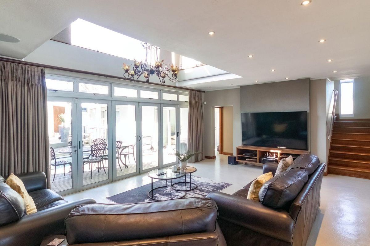 Spacious living room featuring high ceilings with skylights, large glass sliding doors opening to the patio, and a staircase leading to the upper level.