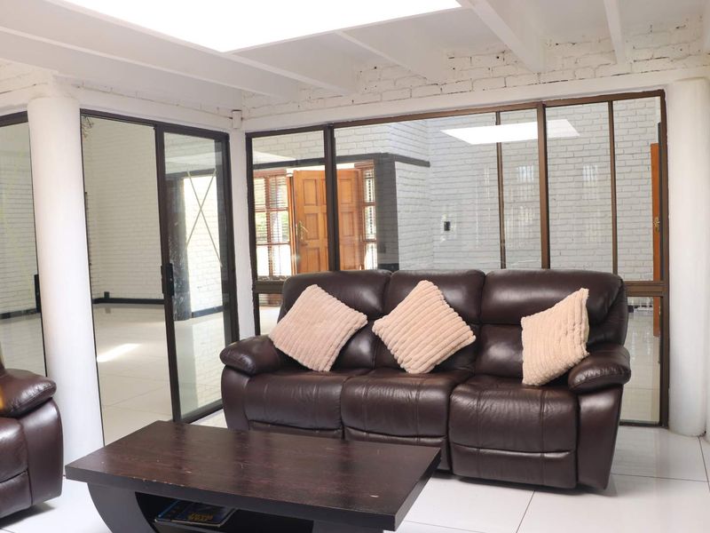 A bright living room featuring white painted exposed brick walls, tiled flooring, and large sliding glass doors that provide ample natural light.