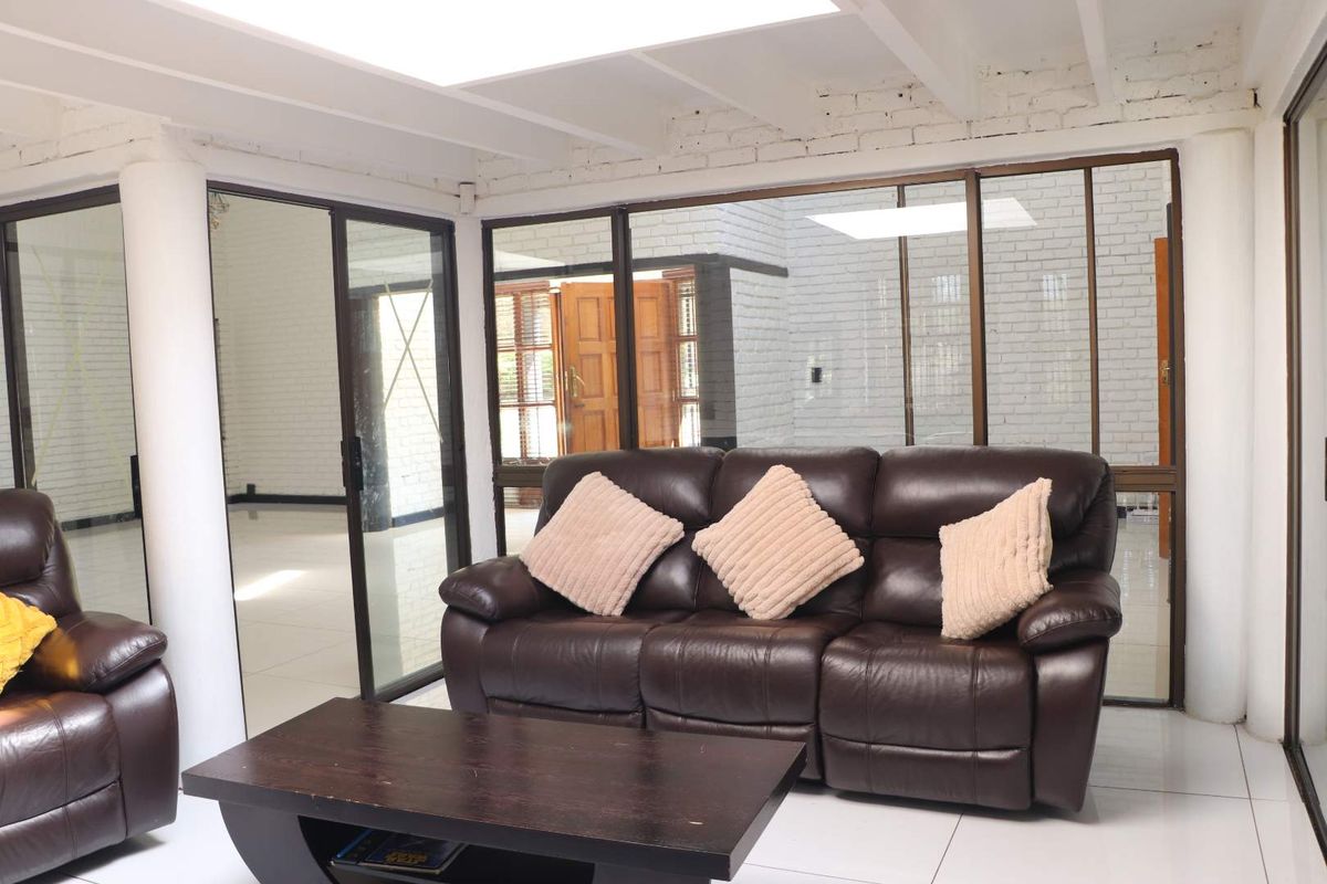 A bright living room featuring white painted exposed brick walls, tiled flooring, and large sliding glass doors that provide ample natural light.