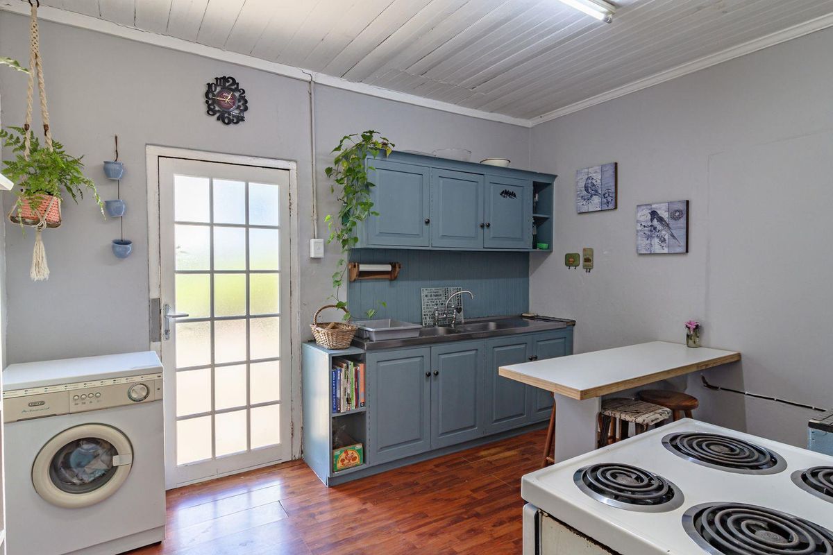A functional kitchen area featuring blue cabinetry, a stainless steel sink, and a glass-paneled exterior door with wood-look flooring.