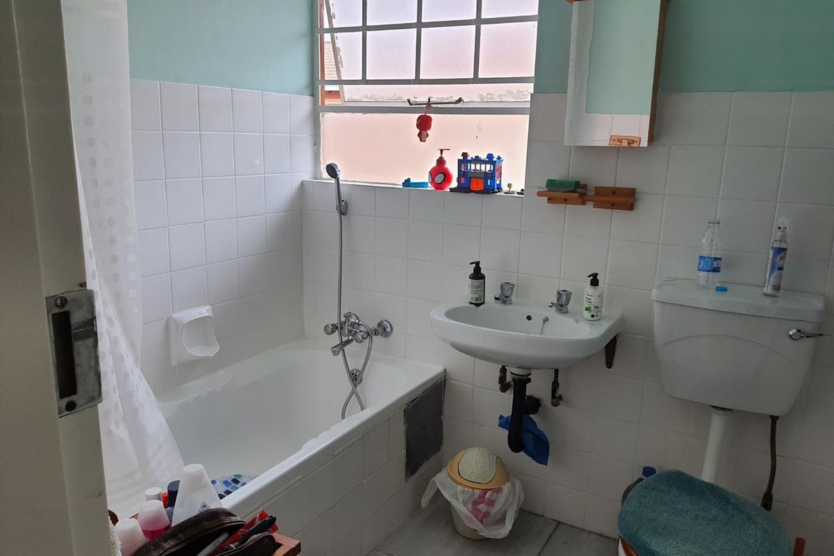 A functional bathroom featuring a bathtub, wall-mounted basin, and toilet with classic white wall tiling and natural light from a window.