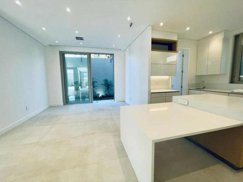 Modern open-plan kitchen and living area featuring sleek cabinetry, stone countertops, recessed lighting, and large sliding glass doors leading to a private courtyard.