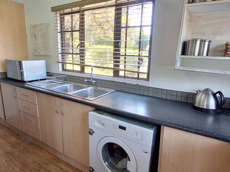Functional kitchen featuring laminate cabinetry, a stainless steel double sink, tiled splashback, and timber flooring, offering a practical layout with integrated laundry space.