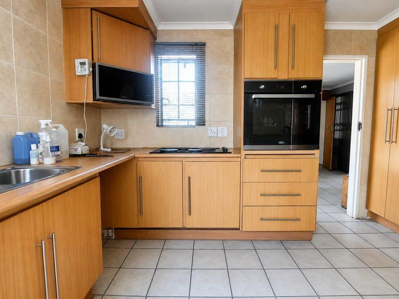 A functional kitchen featuring light wood cabinetry, built-in oven and microwave, electric hob, and tiled flooring with a neutral splashback.