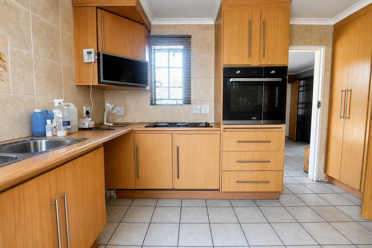 A functional kitchen featuring light wood cabinetry, built-in oven and microwave, electric hob, and tiled flooring with a neutral splashback.