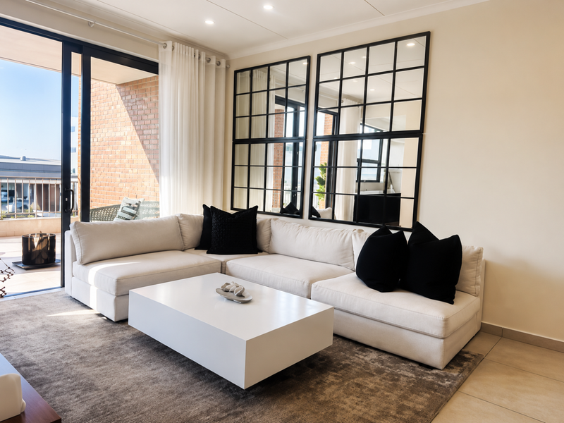 A bright and modern living room featuring large window mirrors, recessed lighting, and a sliding glass door leading to an outdoor balcony area.
