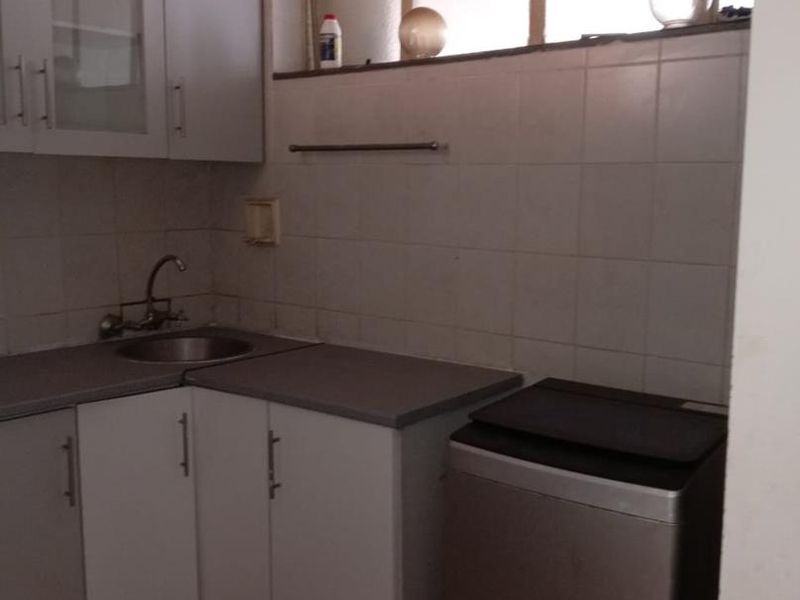 A functional laundry area featuring built-in cabinetry, a stainless steel sink, tiled backsplash, and tiled flooring.