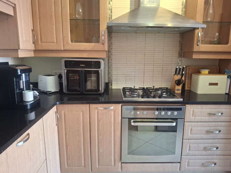 A functional kitchen featuring light wood cabinetry, black granite countertops, a gas hob, built-in oven, and a stainless steel extractor fan.