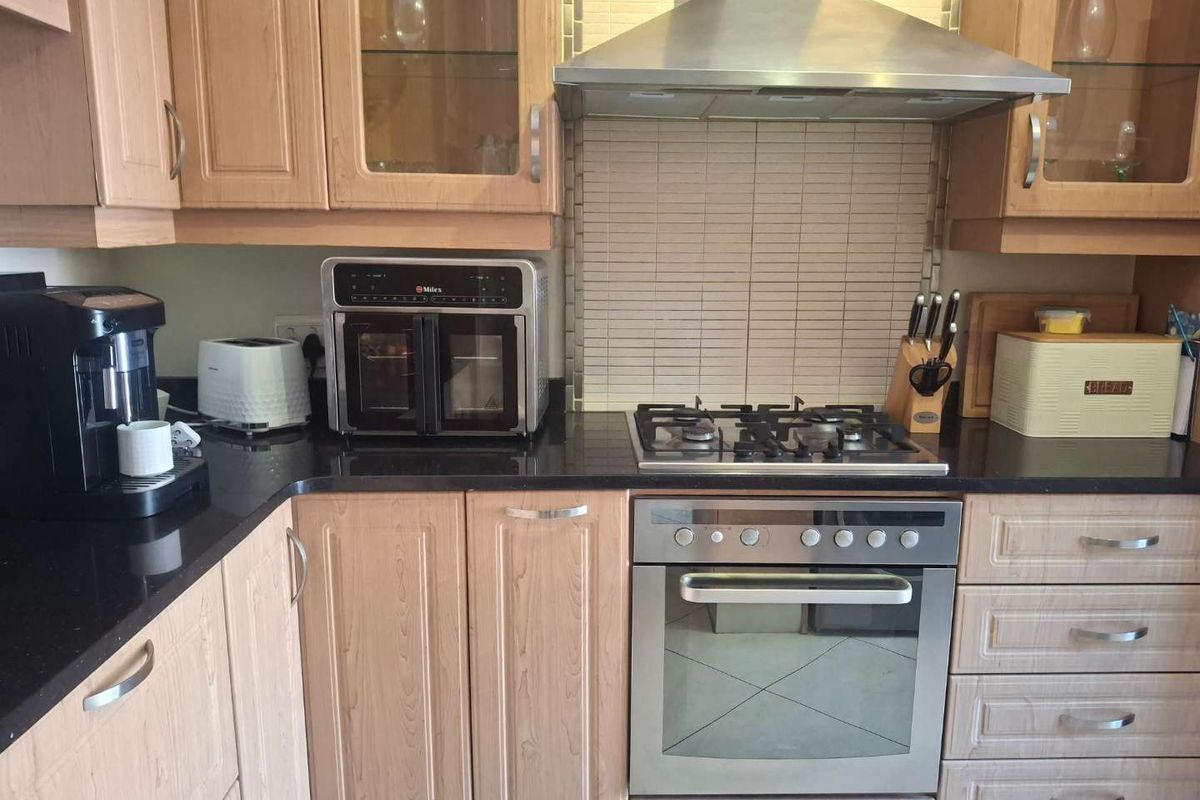 A functional kitchen featuring light wood cabinetry, black granite countertops, a gas hob, built-in oven, and a stainless steel extractor fan.