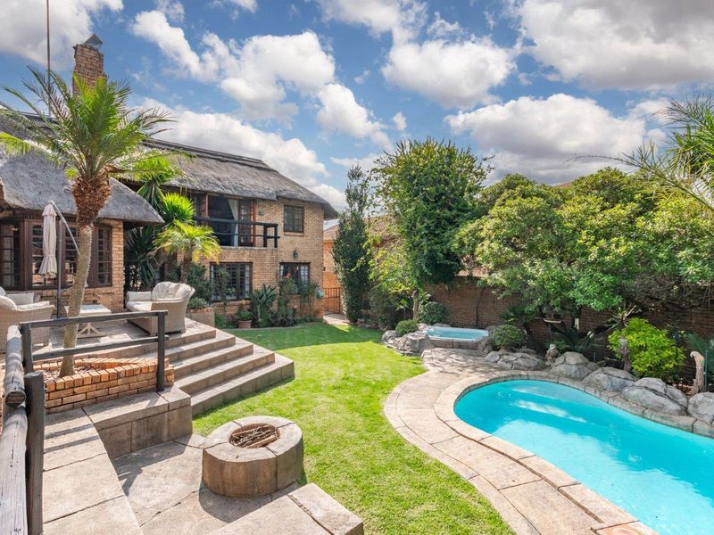 Rear exterior view featuring a thatched roof cluster home, raised patio, built-in fire pit, landscaped garden, and a swimming pool.