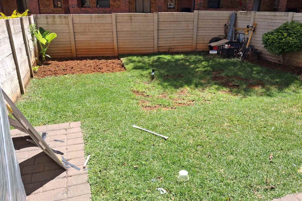 A private rear garden area featuring a paved walkway, lawn space, and perimeter boundary walls.