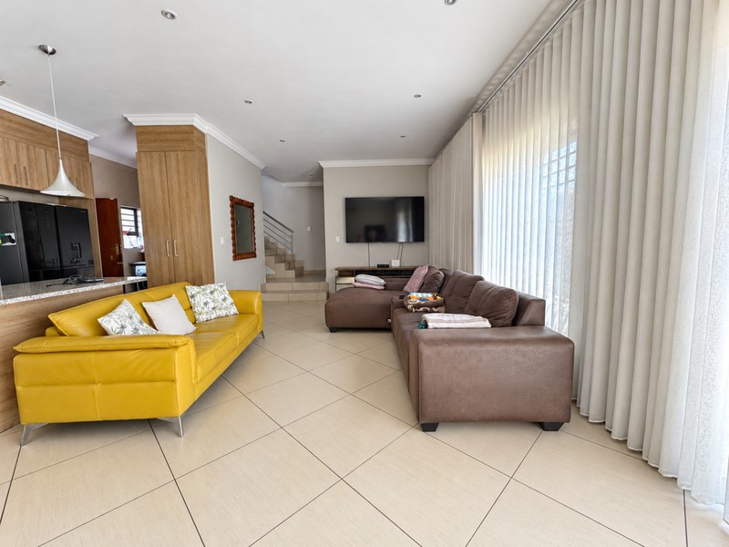 Spacious open-plan living area featuring modern cabinetry, stone countertops, large ceramic floor tiles, and abundant natural light through floor-to-ceiling vertical blinds.