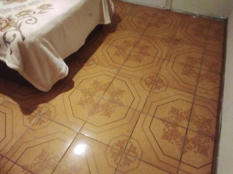 A bedroom featuring dated patterned ceramic floor tiles, showing signs of wear and age.