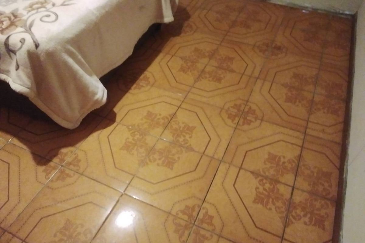 A bedroom featuring dated patterned ceramic floor tiles, showing signs of wear and age.