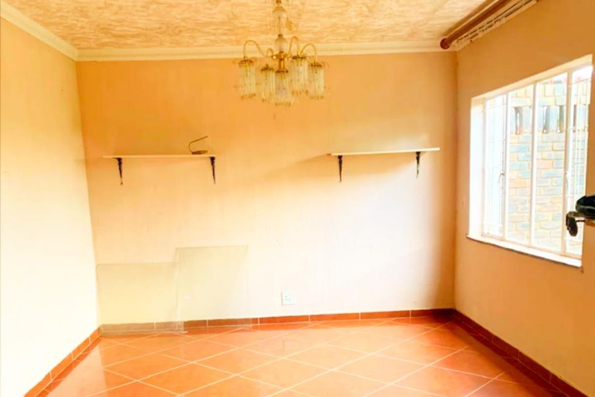 An empty living room featuring tiled flooring, a decorative chandelier, and wall-mounted shelving units under a textured ceiling.