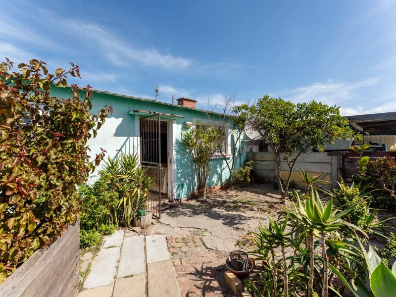Rear exterior view of the property featuring a small garden area, concrete and brick paving, and a security gate entrance.