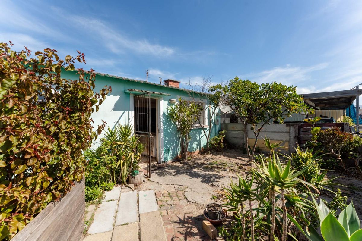 Rear exterior view of the property featuring a small garden area, concrete and brick paving, and a security gate entrance.