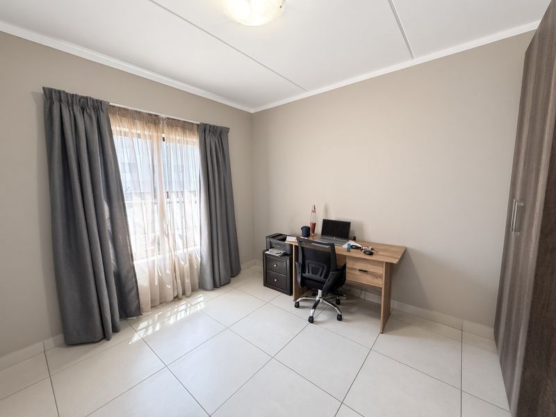 A bright bedroom featuring neutral wall tones, large format floor tiles, and a built-in wardrobe, currently utilized as a home office space.