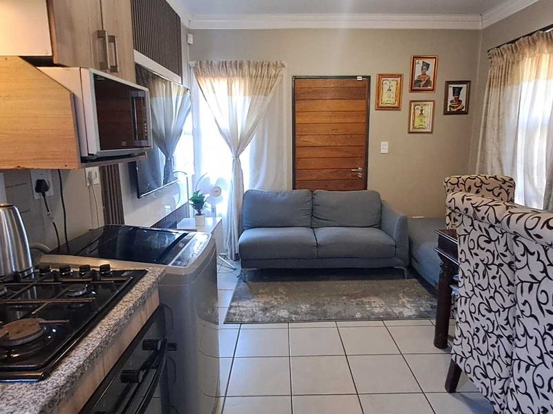 Open-plan living area featuring a functional kitchen with granite countertops, gas hob, and built-in oven, seamlessly flowing into the dining and lounge space.