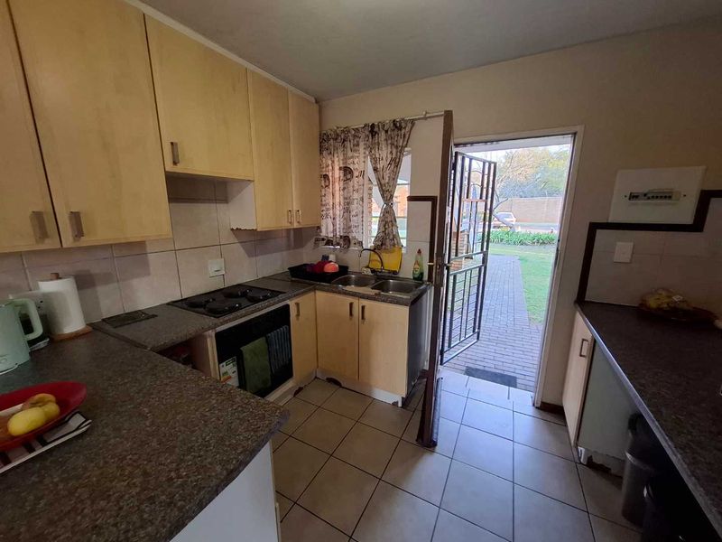 Functional kitchen featuring laminate cabinetry, built-in oven and hob, double sink, and direct access to the exterior through a security gate.