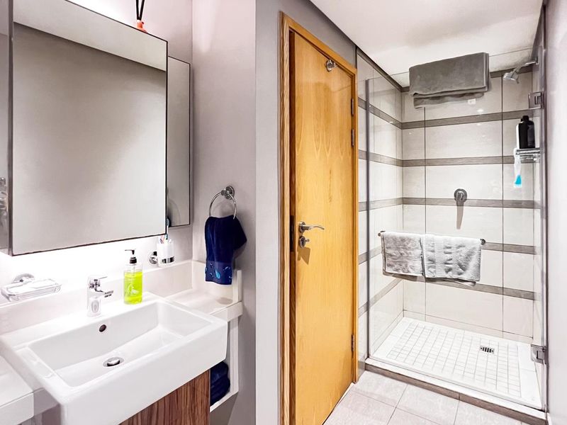 Modern bathroom featuring a glass-enclosed walk-in shower, wall-mounted vanity with integrated basin, and a large mirror with under-cabinet lighting.