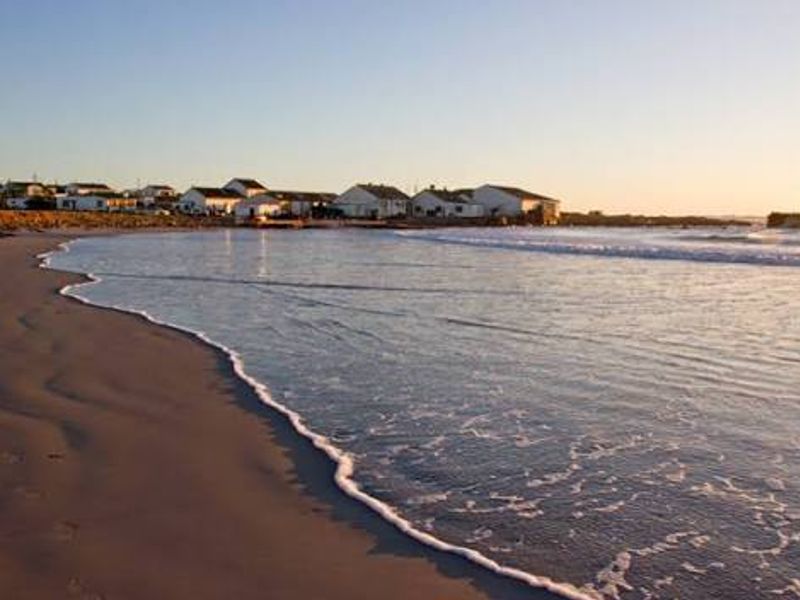 A scenic coastal view overlooking the sandy beach and ocean with residential properties visible in the background.