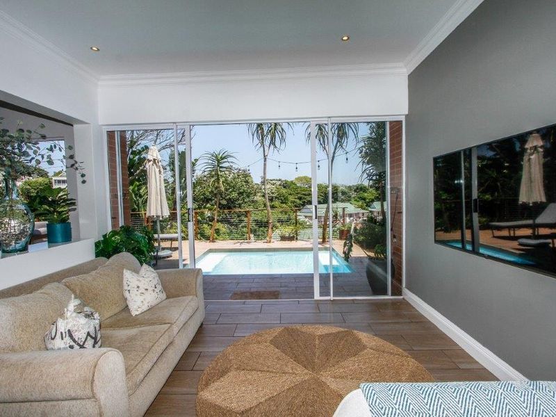 Bright living room featuring large sliding glass doors that open onto a patio with a swimming pool and garden views.
