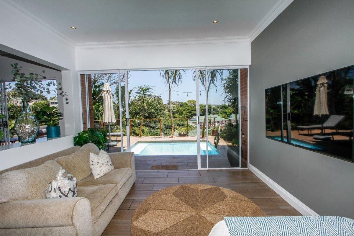 Bright living room featuring large sliding glass doors that open onto a patio with a swimming pool and garden views.