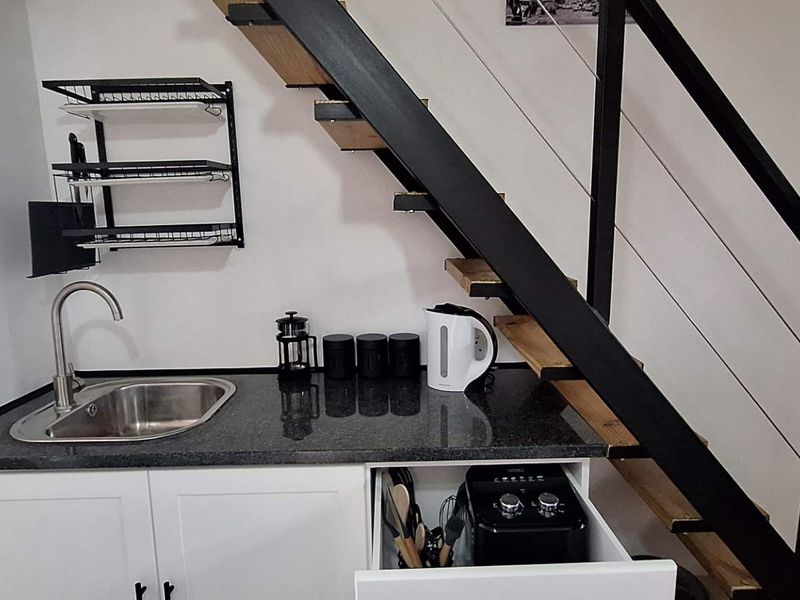 Compact kitchenette featuring a granite countertop, stainless steel sink, and built-in cabinetry, conveniently located beneath a modern staircase.