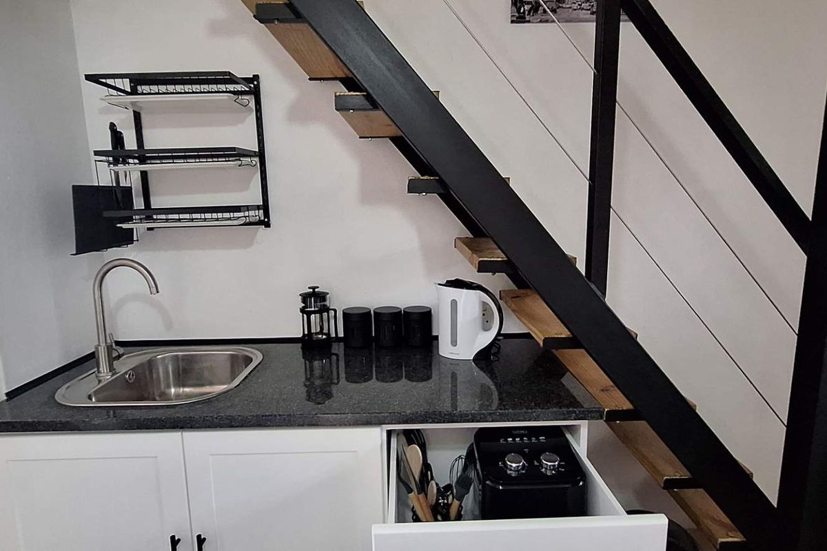 Compact kitchenette featuring a granite countertop, stainless steel sink, and built-in cabinetry, conveniently located beneath a modern staircase.