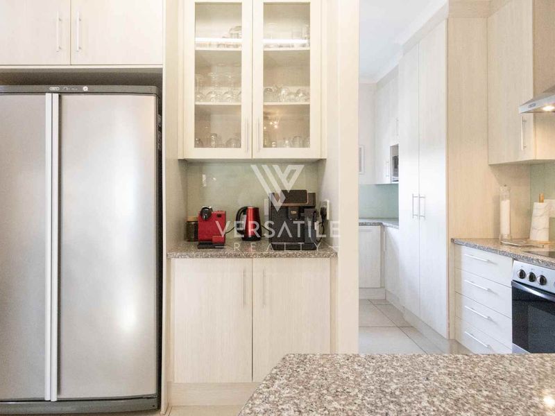 Modern kitchen featuring granite countertops, ample built-in cabinetry, glass-front display units, and integrated stainless steel appliances, with an adjacent scullery area.