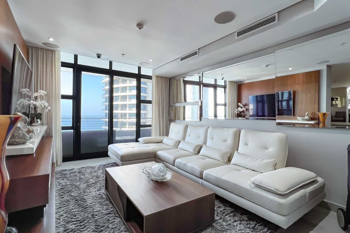 A modern living room featuring floor-to-ceiling windows, integrated ceiling speakers, ducted air conditioning, and a large wall-mounted mirror.