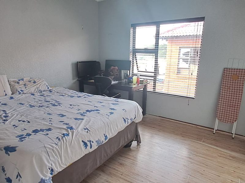 A bedroom featuring laminate flooring, built-in cupboards, and a window with venetian blinds, offering a functional living space.
