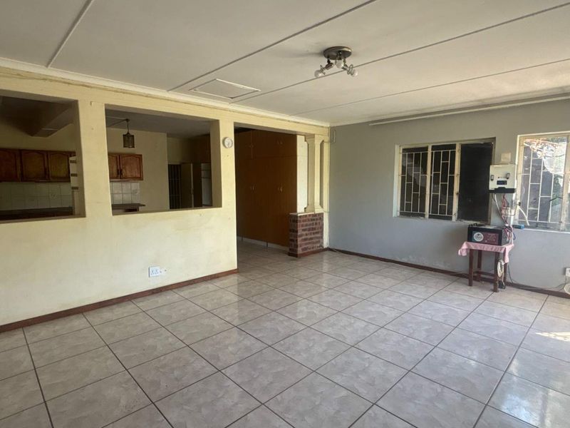 Spacious open-plan living area featuring tiled flooring, built-in storage, and a convenient pass-through window connecting to the kitchen area.