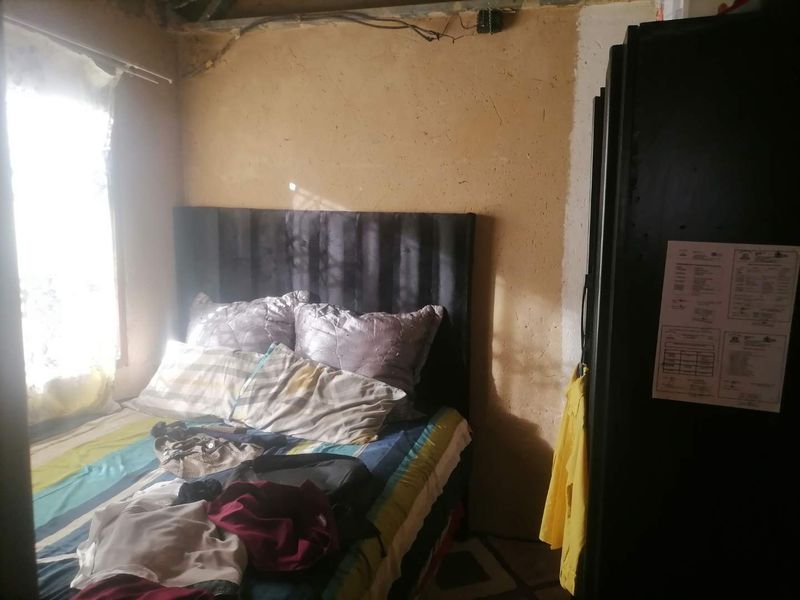A bedroom space requiring significant renovation, featuring unfinished wall textures and exposed electrical wiring near the ceiling.