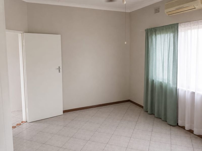 A clean, vacant bedroom featuring neutral wall tones, tiled flooring, an integrated air conditioning unit, and a ceiling fan.