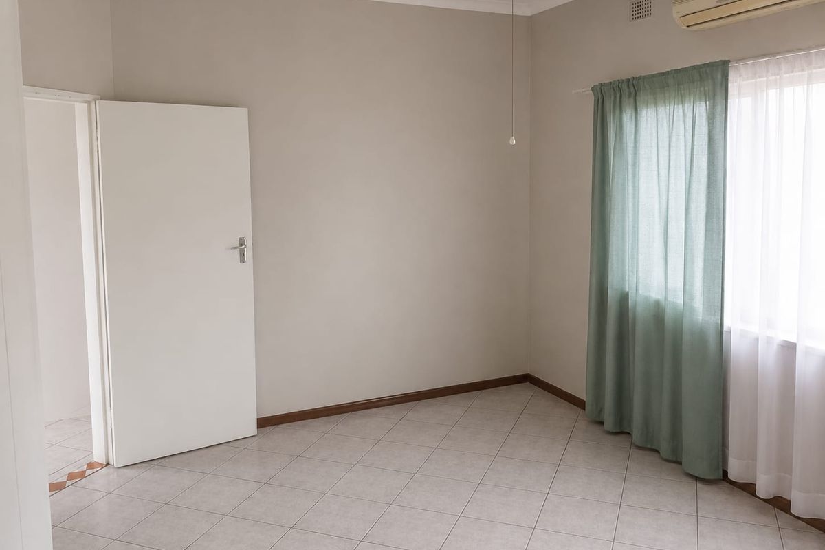 A clean, vacant bedroom featuring neutral wall tones, tiled flooring, an integrated air conditioning unit, and a ceiling fan.