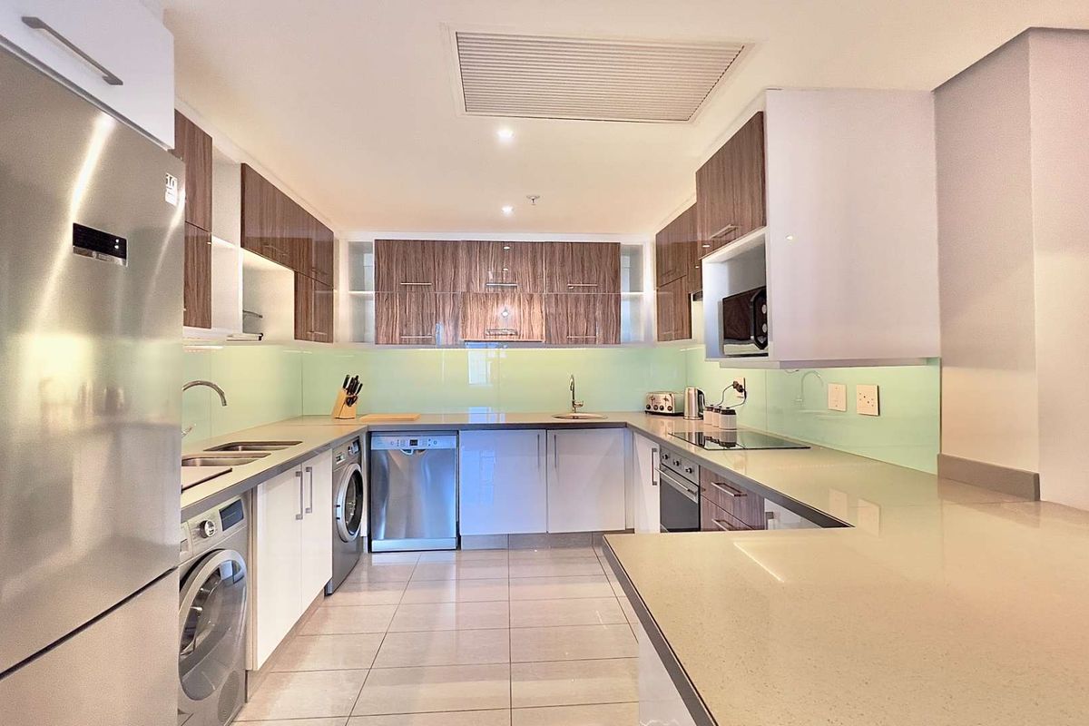 Modern U-shaped kitchen featuring high-gloss cabinetry, stone countertops, glass splashback, integrated appliances, and recessed lighting in a clean, contemporary finish.