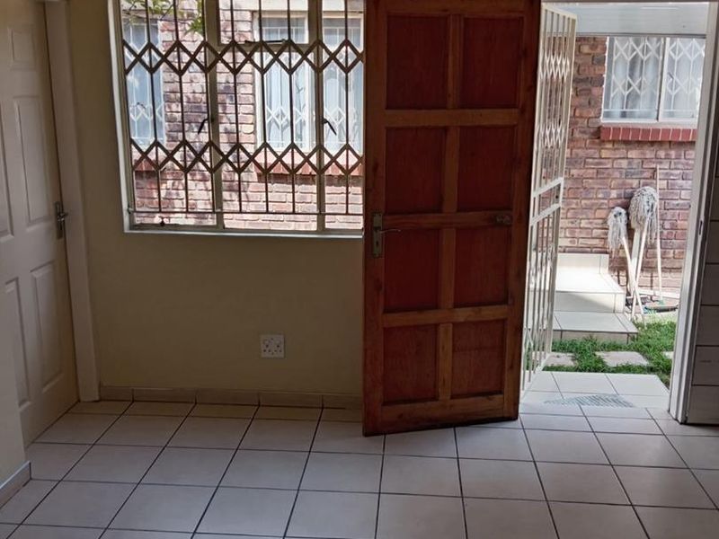An empty living area featuring tiled flooring, a timber door, and security gates leading to an outdoor space.
