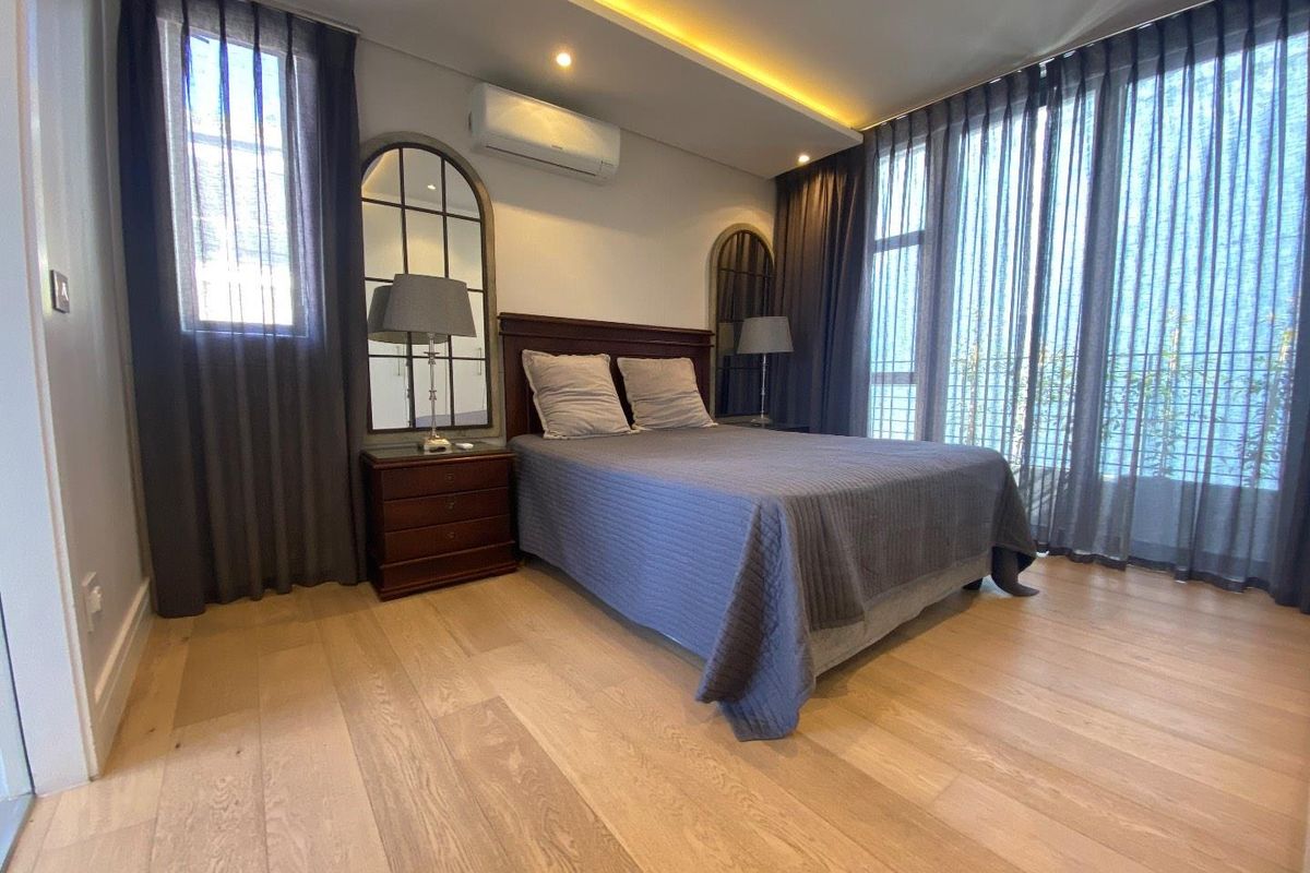 A well-appointed bedroom featuring modern engineered timber flooring, recessed ceiling lighting, and a split-system air conditioning unit with access to a balcony.