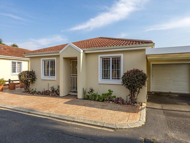 Front elevation of a single-story residential house featuring a tiled roof, paved driveway, integrated garage, and security features on windows and entrance.