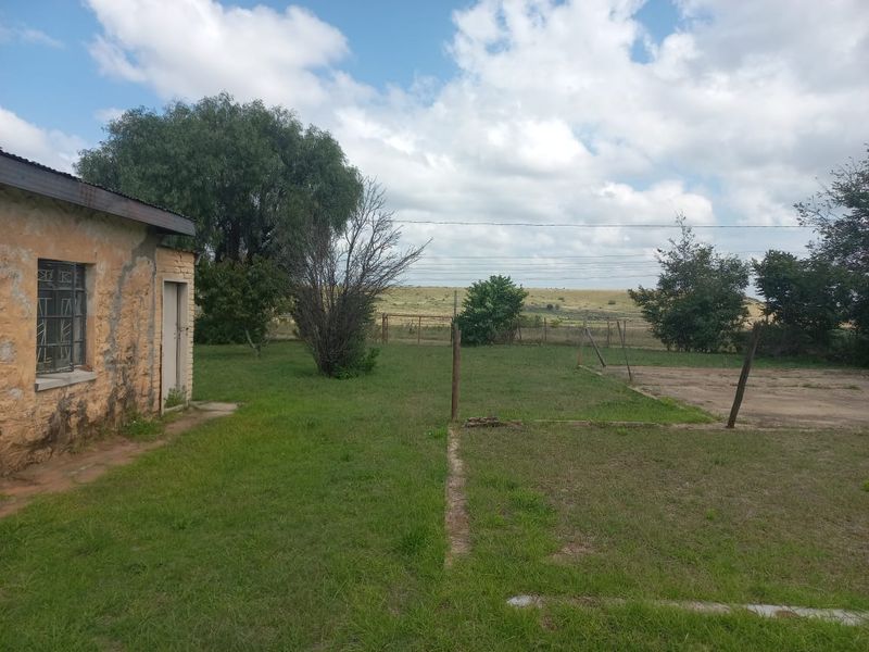 Rear view of the property showing the exterior wall with security bars, surrounding garden area, and open landscape views.