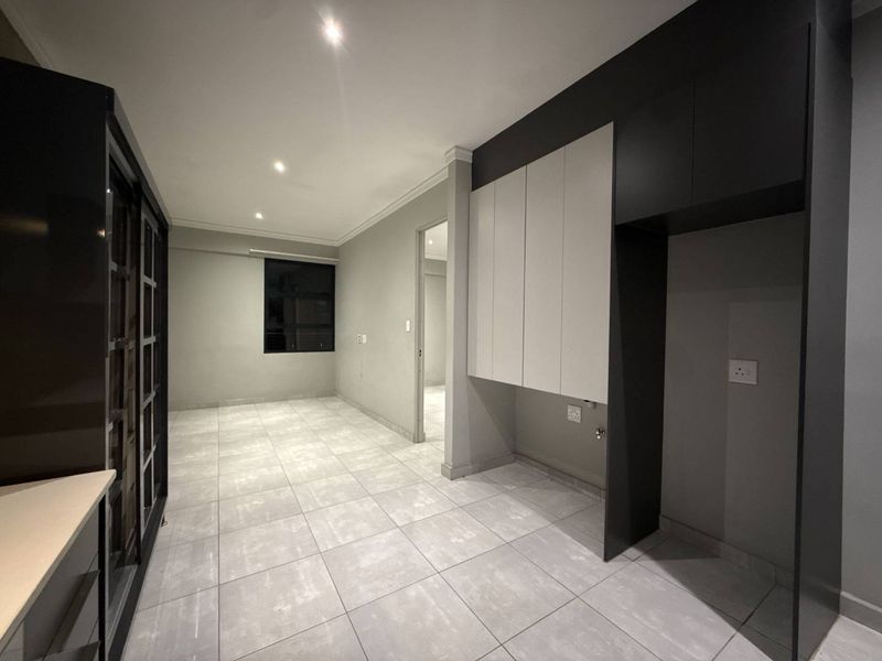 A modern, empty kitchen area featuring sleek built-in cabinetry, neutral tiled flooring, and recessed lighting, providing a clean and functional space ready for appliances.