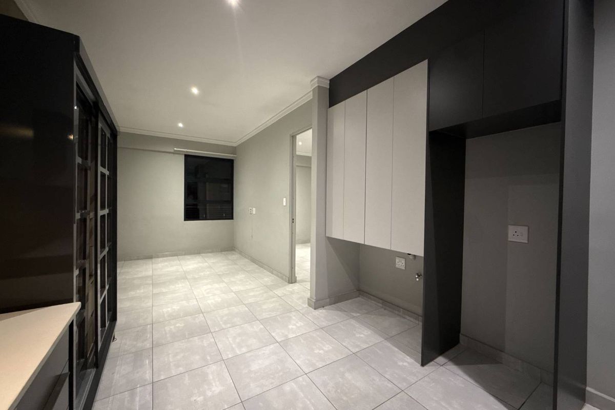 A modern, empty kitchen area featuring sleek built-in cabinetry, neutral tiled flooring, and recessed lighting, providing a clean and functional space ready for appliances.