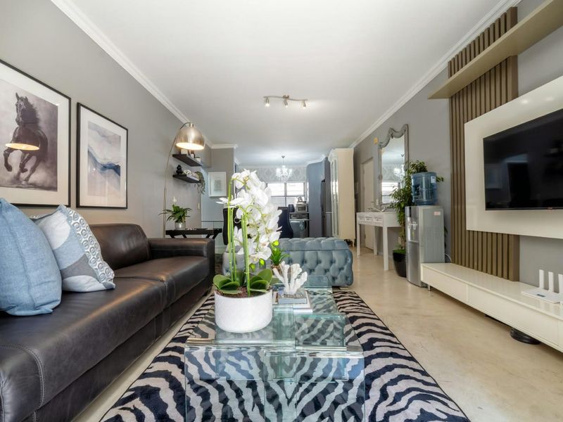 A well-maintained open-plan living area featuring a modern media wall, decorative paneling, and neutral tiled flooring, creating a cohesive and inviting space.