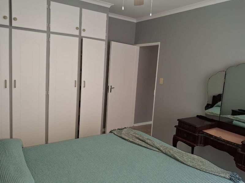 A bedroom featuring built-in cupboards with overhead storage and a ceiling fan, finished with neutral grey walls and coving.